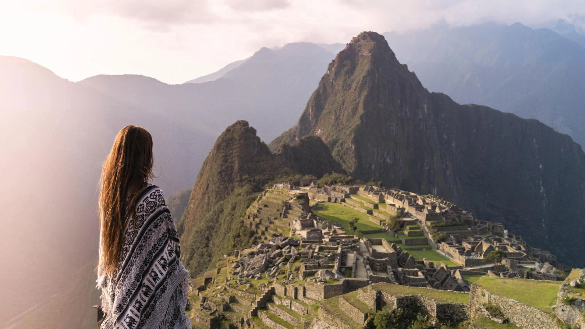 Female tourist admiring the breathtaking view of Machu Picchu surrounded by lush mountains | Andean Travel Experience