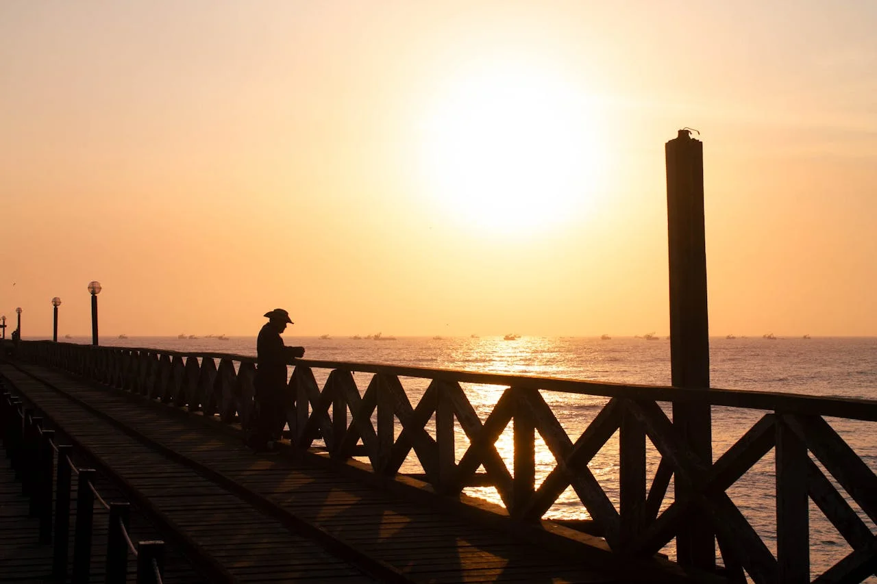 Wooden pier at Pimentel Beach extending over the ocean, with traditional reed boats and waves breaking beneath the long coastal walkway. | Andean Travel Experience Wooden pier at Pimentel Beach extending over the ocean, with traditional reed boats and waves breaking beneath the long coastal walkway. | Andean Travel Experience