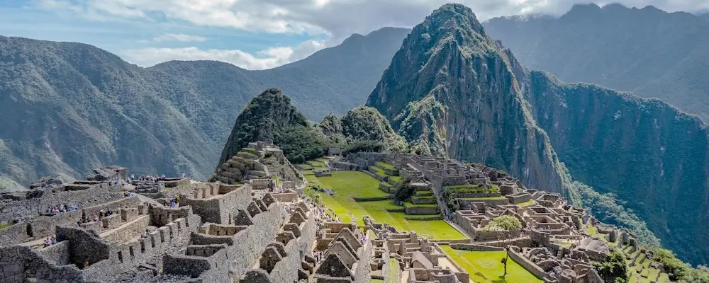 Panoramic view of Machu Picchu with the iconic Huayna Picchu mountain in the background, surrounded by lush green Andean peaks and misty clouds. | Andean Travel Experience