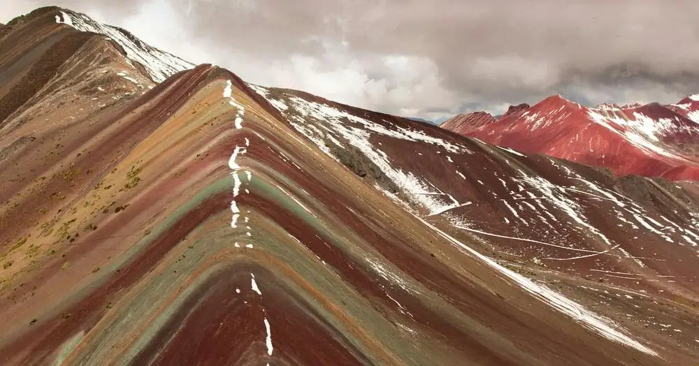 Striped Rainbow Mountain displaying natural red, yellow, green, and purple mineral layers with hikers walking along the scenic Andean trail. | Andean Travel Experience