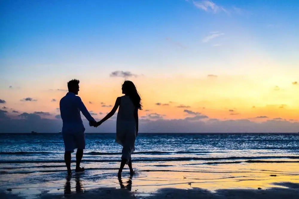 Romantic couple walking along a serene beach in Peru during their honeymoon, with soft waves, golden light, and a peaceful coastal backdrop. | Andean Travel Experience