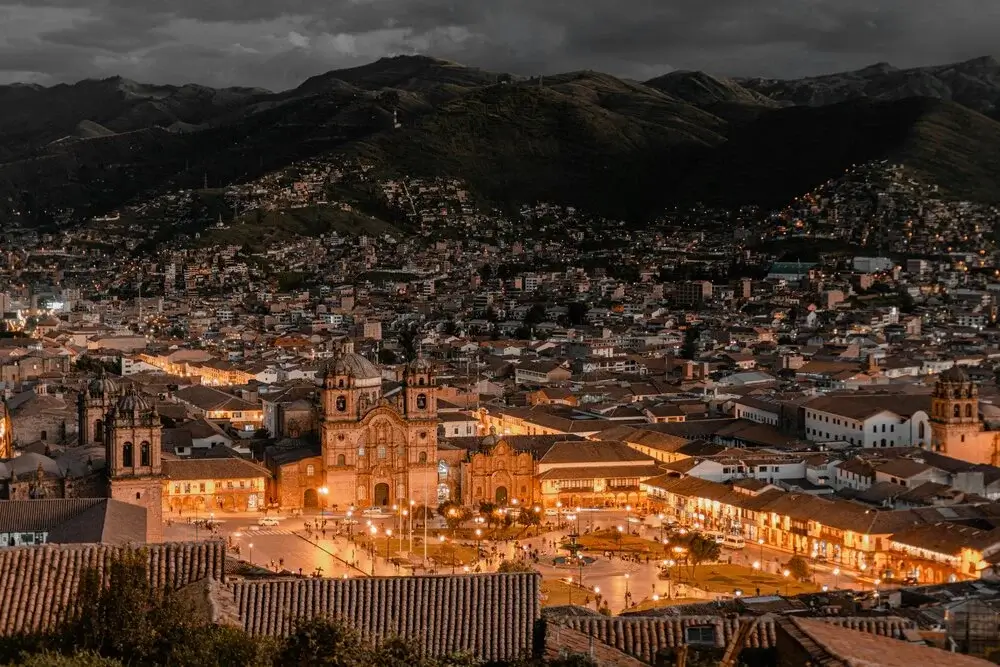Night aerial view of Cusco city center with illuminated Plaza de Armas, colonial architecture, and surrounding Andes mountains | Andean Travel Experience