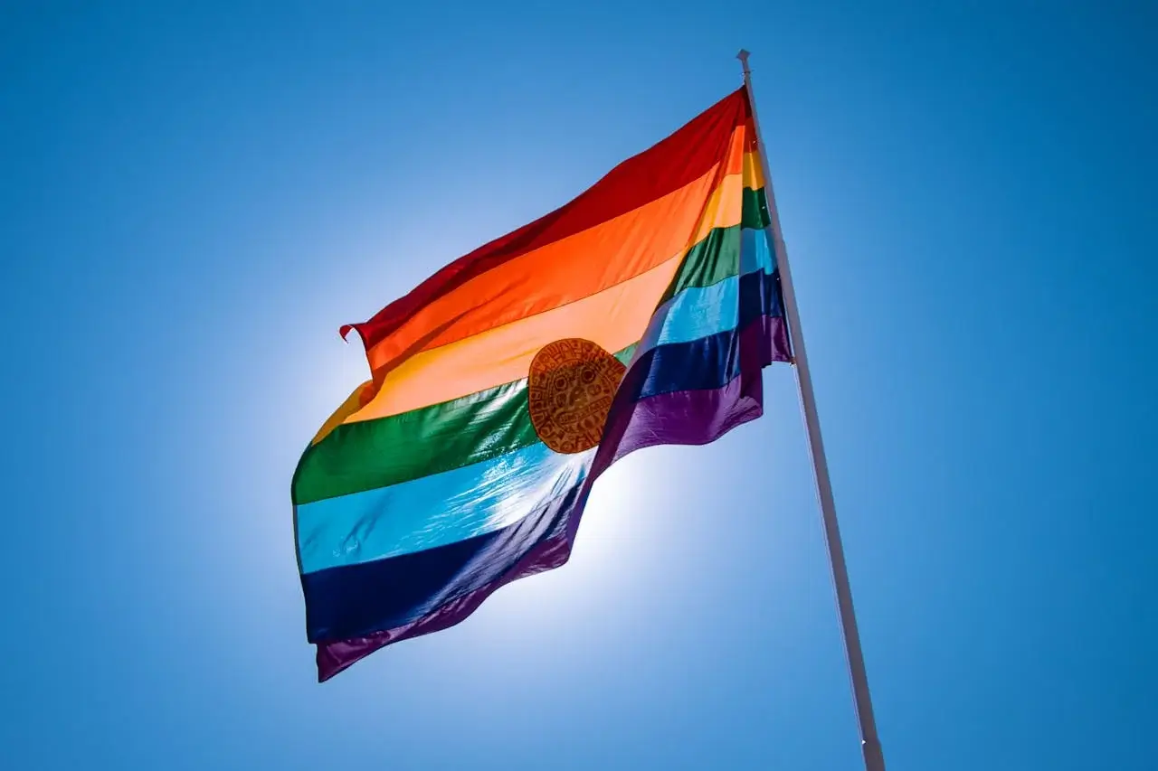 Rainbow flag of Cusco fluttering under a bright sunny blue sky, symbolizing the vibrant culture and heritage of the Andean region in Peru. | Andean Travel Experience