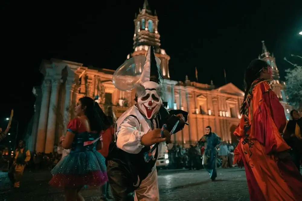 Person in a black and white clown Halloween costume standing in front of Arequipa Cathedral at night | Andean Travel Experience