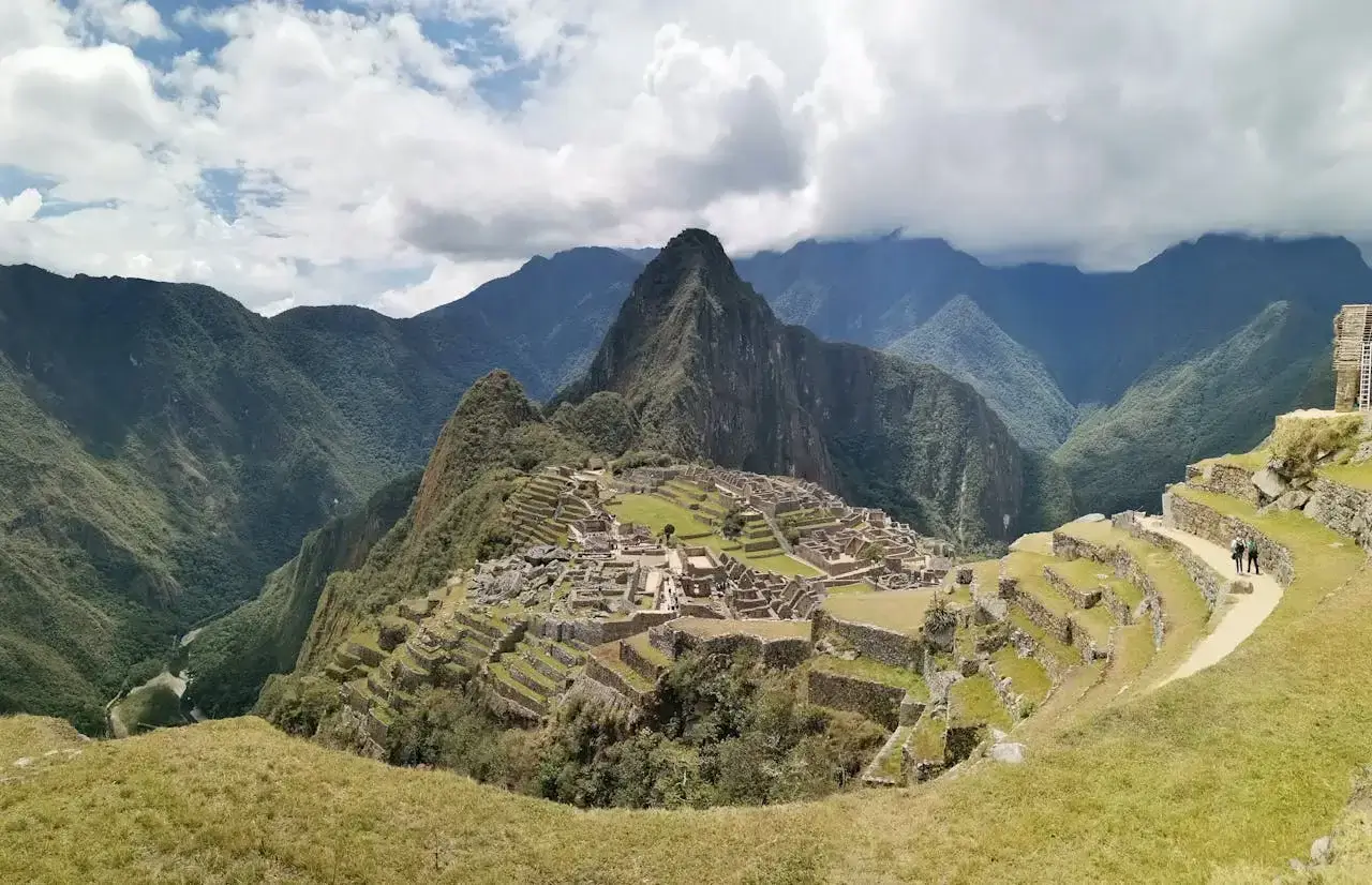 Panoramic view of Machu Picchu citadel surrounded by lush green mountains under a clear sky. | Andean Travel Experience