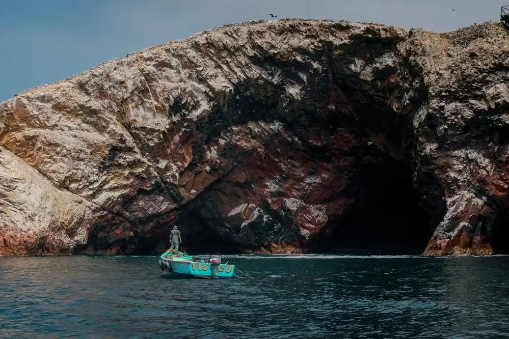 Tourist boat sailing through the blue waters of Paracas Bay, Peru, with rocky islands and seabirds in the background. | Andean Travel Experience Tourist boat sailing through the blue waters of Paracas Bay, Peru, with rocky islands and seabirds in the background. | Andean Travel Experience