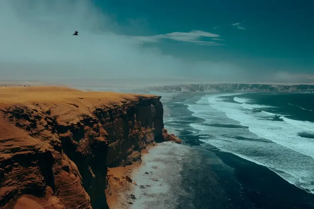 Panoramic view of the Paracas coastline, where desert mountains meet the deep blue Pacific Ocean under a clear sky. | Andean Travel Experience Panoramic view of the Paracas coastline, where desert mountains meet the deep blue Pacific Ocean under a clear sky. | Andean Travel Experience