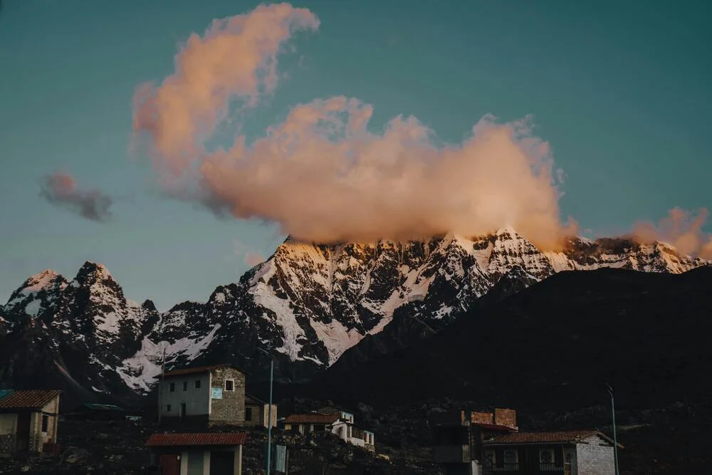 Snow-capped mountain in Peru glowing under a golden sunset, with soft clouds drifting across the peak. | Andean Travel Experience