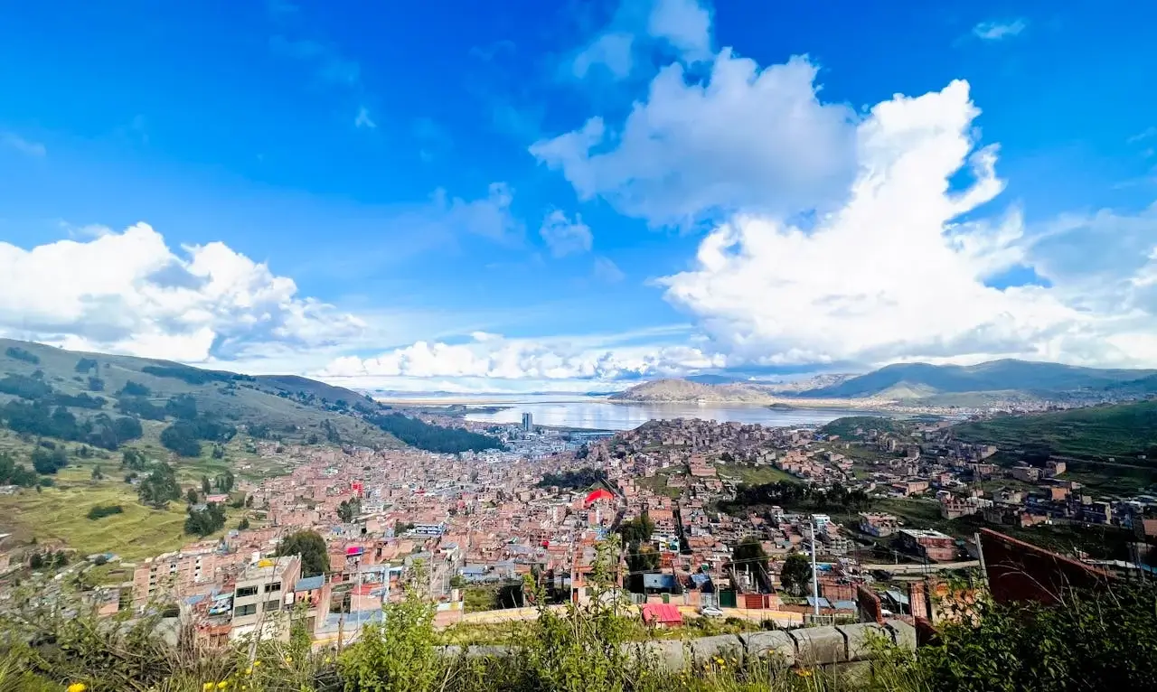Aerial view of Puno city overlooking the shores of Lake Titicaca, surrounded by the majestic Andes mountains. | Andean Travel Experience