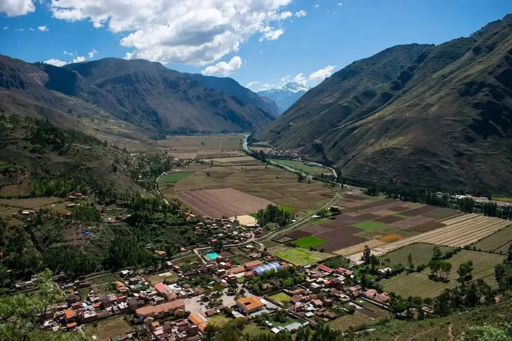 Panoramic view of the Sacred Valley in Peru, with green terraced fields, the Urubamba River winding through the valley, and the Andes mountains in the background. | Andean Travel Experience