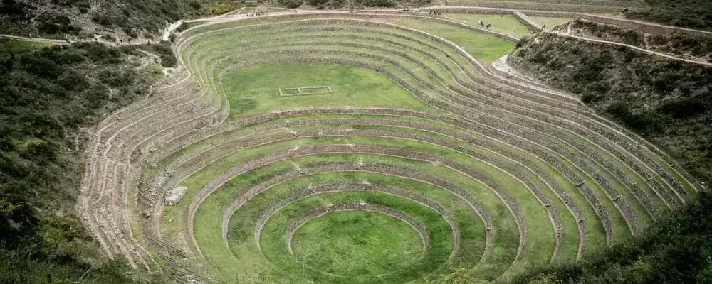 Circular agricultural terraces of Moray in the Sacred Valley, Peru, showcasing ancient Inca engineering set against the Andean mountains under a clear blue sky. | Andean Travel Experience