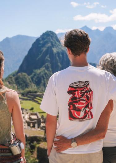 Family relaxing together while enjoying a scenic view of Machu Picchu from a high vantage point, surrounded by green mountains. | Andean Travel Experience