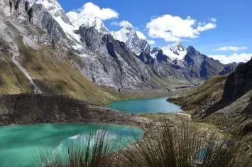 Trekking in the Huayhuash mountains of Peru, with hikers crossing rugged trails surrounded by snow-capped peaks and pristine alpine lakes. | Andean Travel Experience