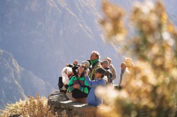 Family relaxing together while enjoying a scenic view of Machu Picchu from a high vantage point, surrounded by green mountains. | Andean Travel Experience