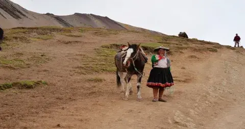 A local woman in traditional attire walking toward Rainbow Mountain, highlighting the cultural heritage of the Andes | Andean Travel Experience