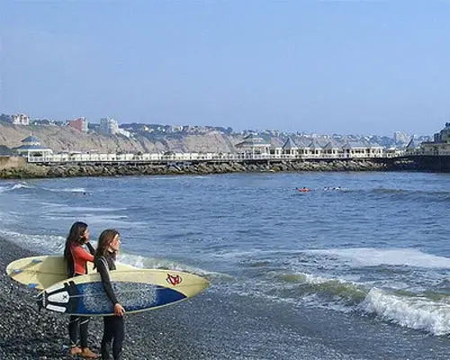 Surfers enjoying the waves at a beach in Lima, Peru, with the ocean and coastline in the background | Andean Travel Experience