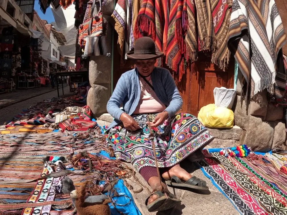 Peruvian woman selling colorful handmade textiles and souvenirs at a traditional market in Peru.. | Andean Travel Experience